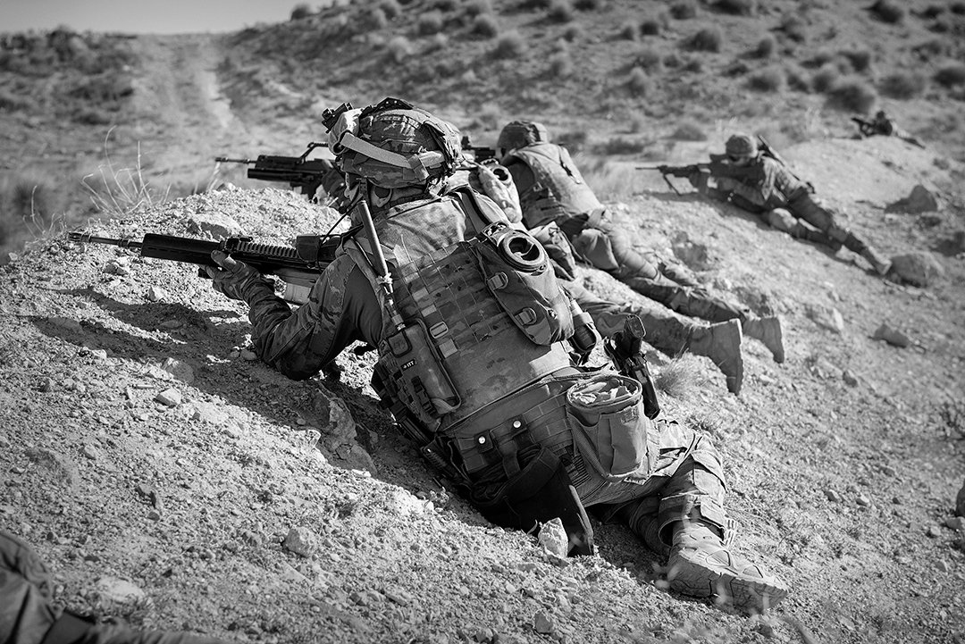 Soldiers lying with their weapons on rocky ground.